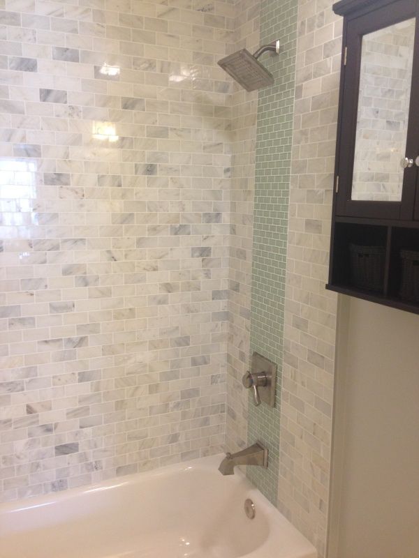 Bathroom with white and gray tiled shower, green accent strip, and dark wood cabinet.