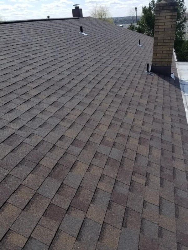 Close-up view of a brown asphalt shingle roof with a brick chimney and vents.