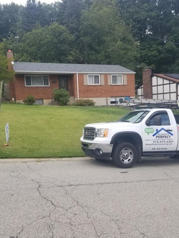 A brick house with a white truck parked in front, likely for roofing work.