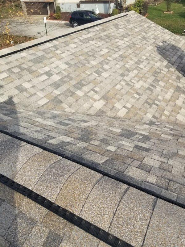 Overhead view of a roof with gray and tan shingles. Black edging frames the roof's edge.