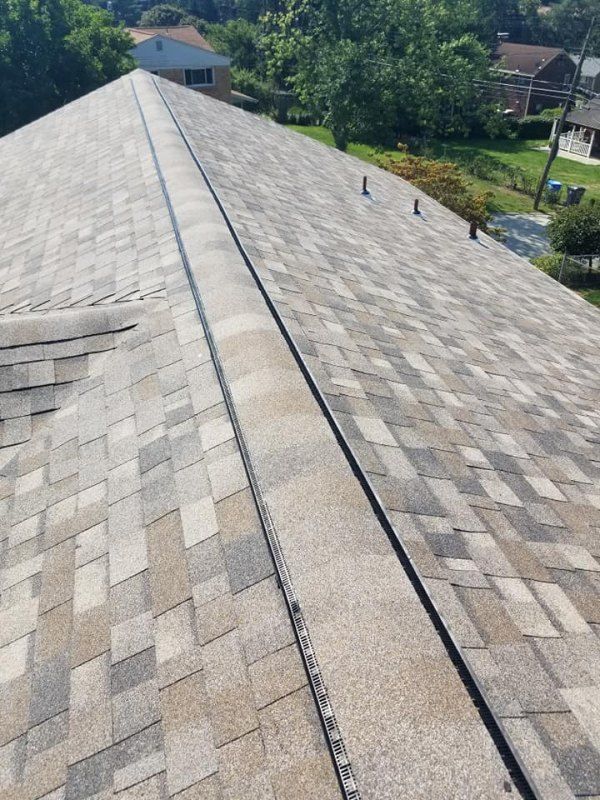 View of a shingled roof with a central ridge. The shingles are various shades of gray and brown.