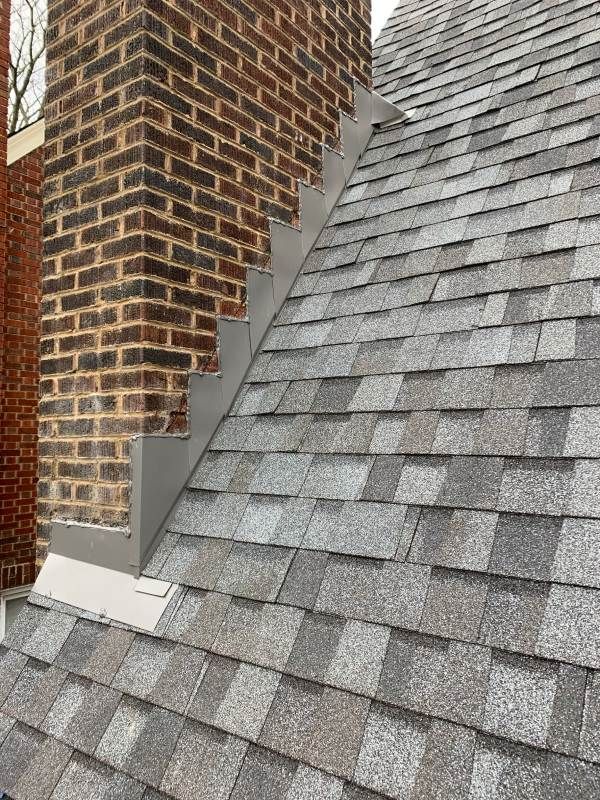 Close-up of a chimney with flashing on a gray shingled roof.