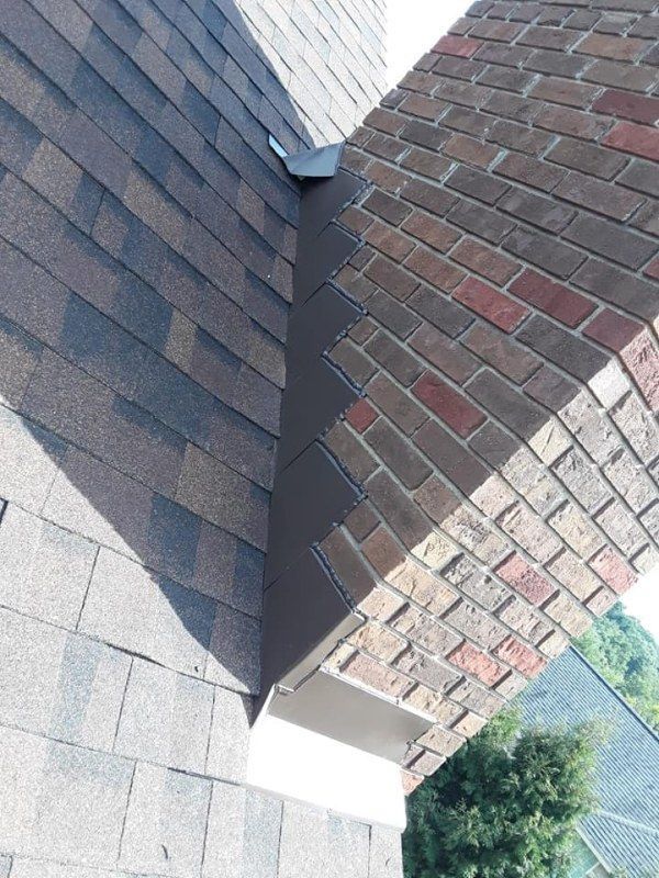Roofing and brick chimney junction with metal flashing.