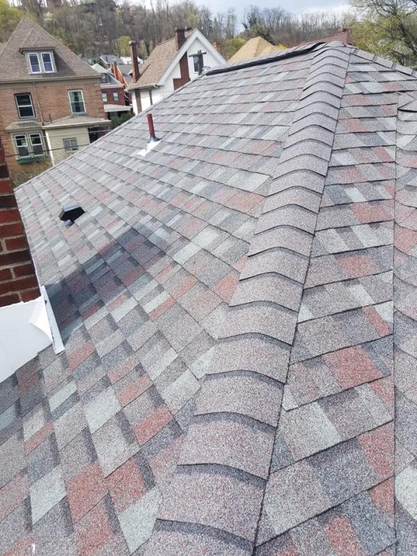 Asphalt shingle roof with varied colors: gray, red, and brown. Buildings in background.