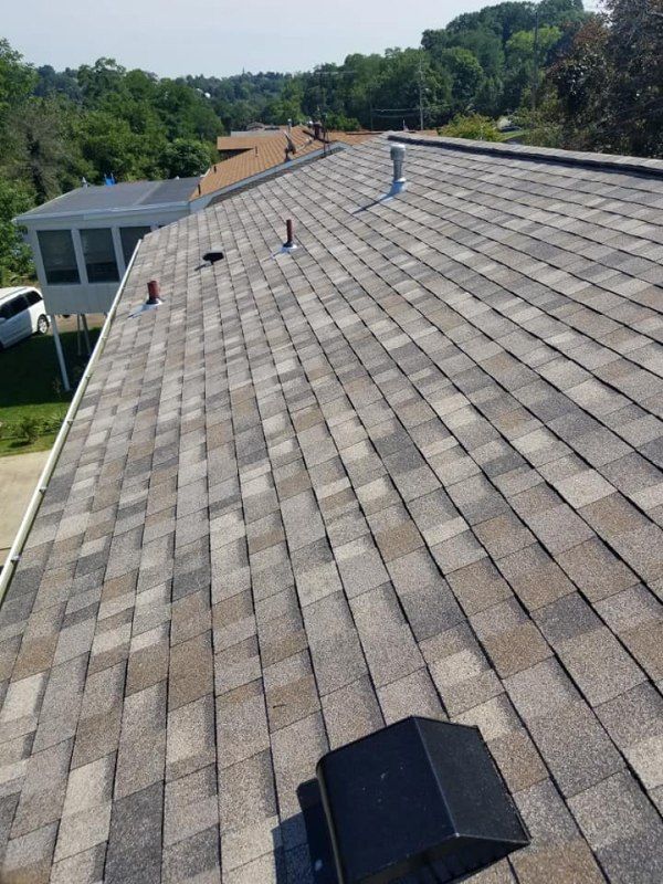 Close-up of a residential roof with gray and brown shingles. Chimney vent and other vents are visible on the roof.