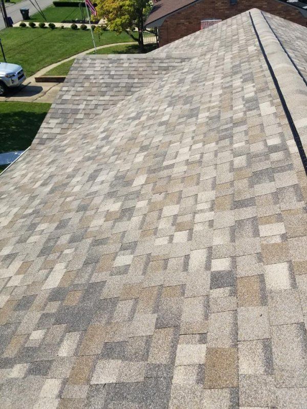Overhead view of a multi-colored shingle roof on a house, angled to show a lawn and street.