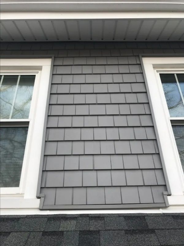 Gray shingle siding between two white-framed windows on a house.