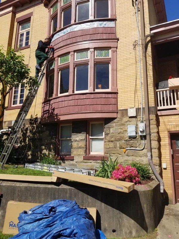 Person on ladder painting exterior bay window on a brick building with dark red trim.