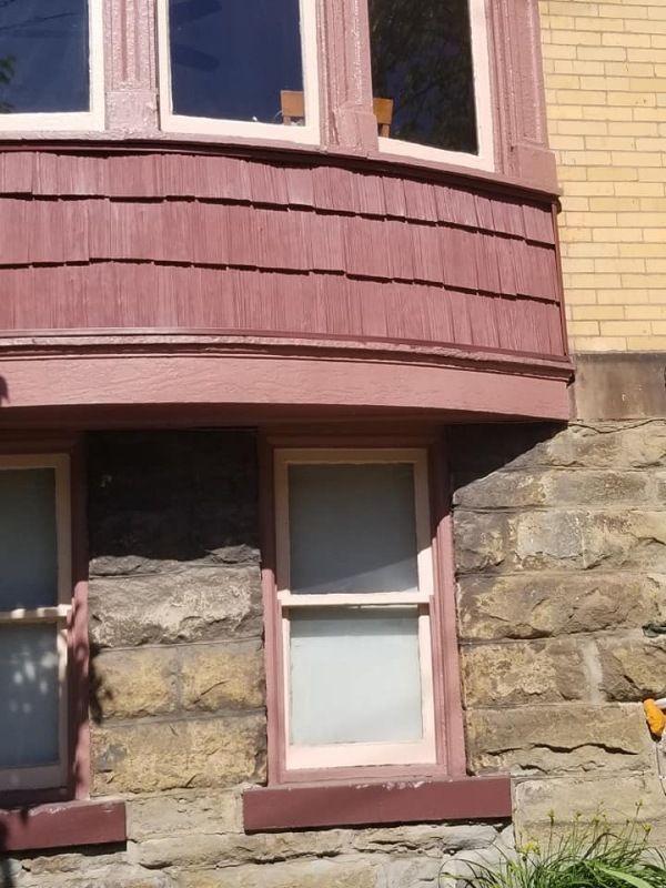 Close-up of a house exterior with stone foundation and red-brown shingle siding, with several windows.