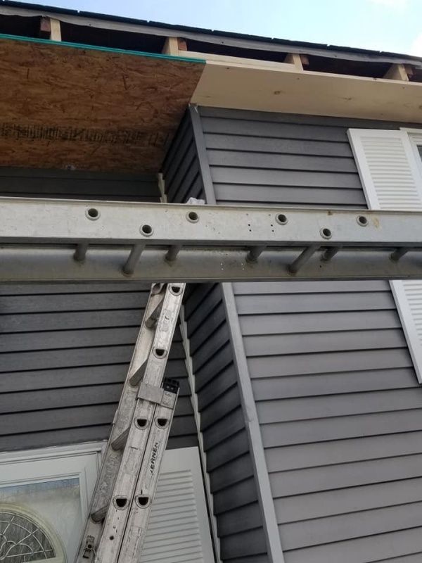 Ladder leaning against a house with gray siding. Construction is in progress near the roofline.