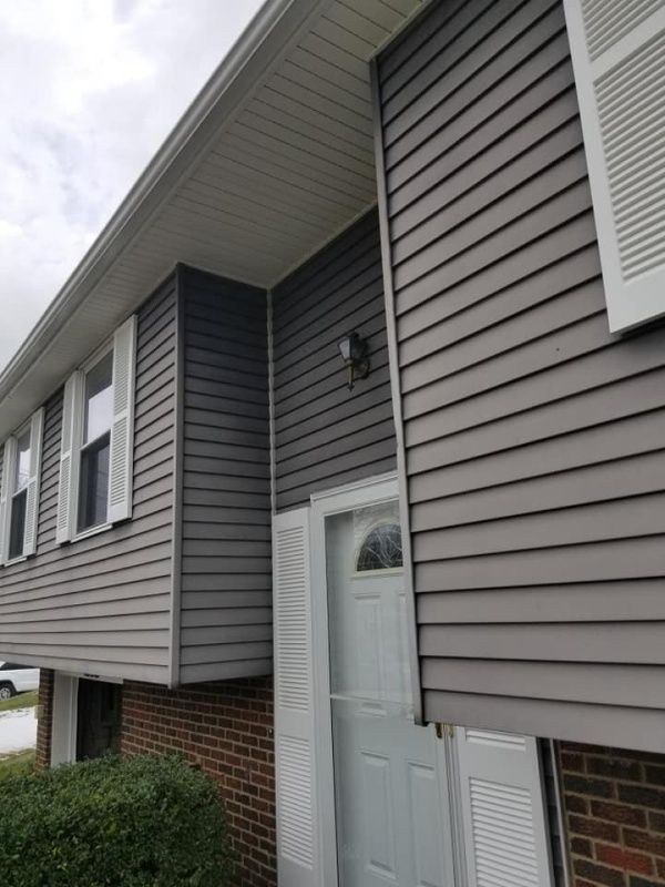 Gray siding and white trim on a house with a brick base; cloudy day.