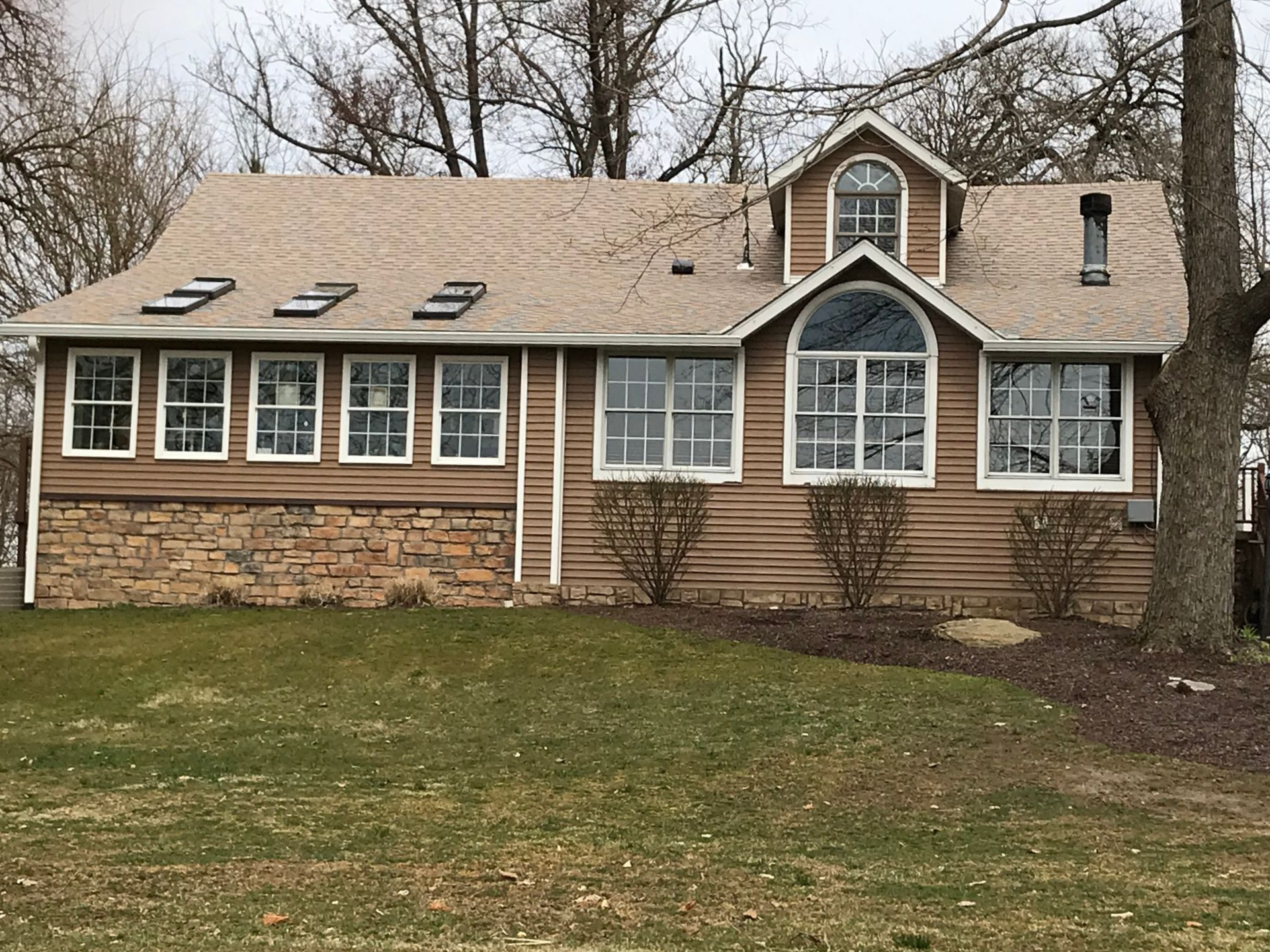 Gray siding on a two-story home with a white garage door, concrete steps, and a black handrail.