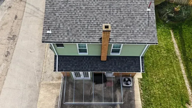 Overhead view of a two-story house with green siding, gray roof, and a brick chimney. A covered patio is at the base.