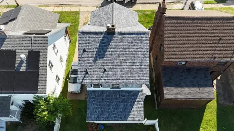 Overhead view of several houses, grey shingled roof in the center, other roofs are lighter, grass and street visible.