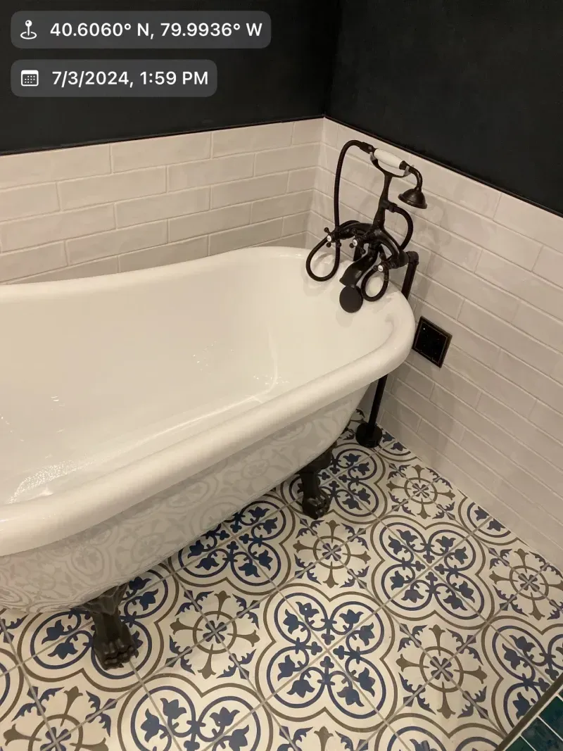 Clawfoot bathtub with dark fixtures in a bathroom with patterned tile floor and white and black walls.