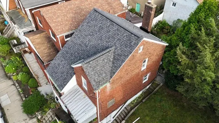 Brick house with dark gray roof, chimney, and surrounding greenery.