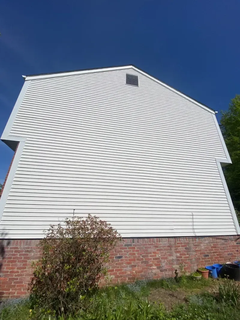 White building with wavy black lines on the side, brick base, blue sky, and a small bush in the foreground.