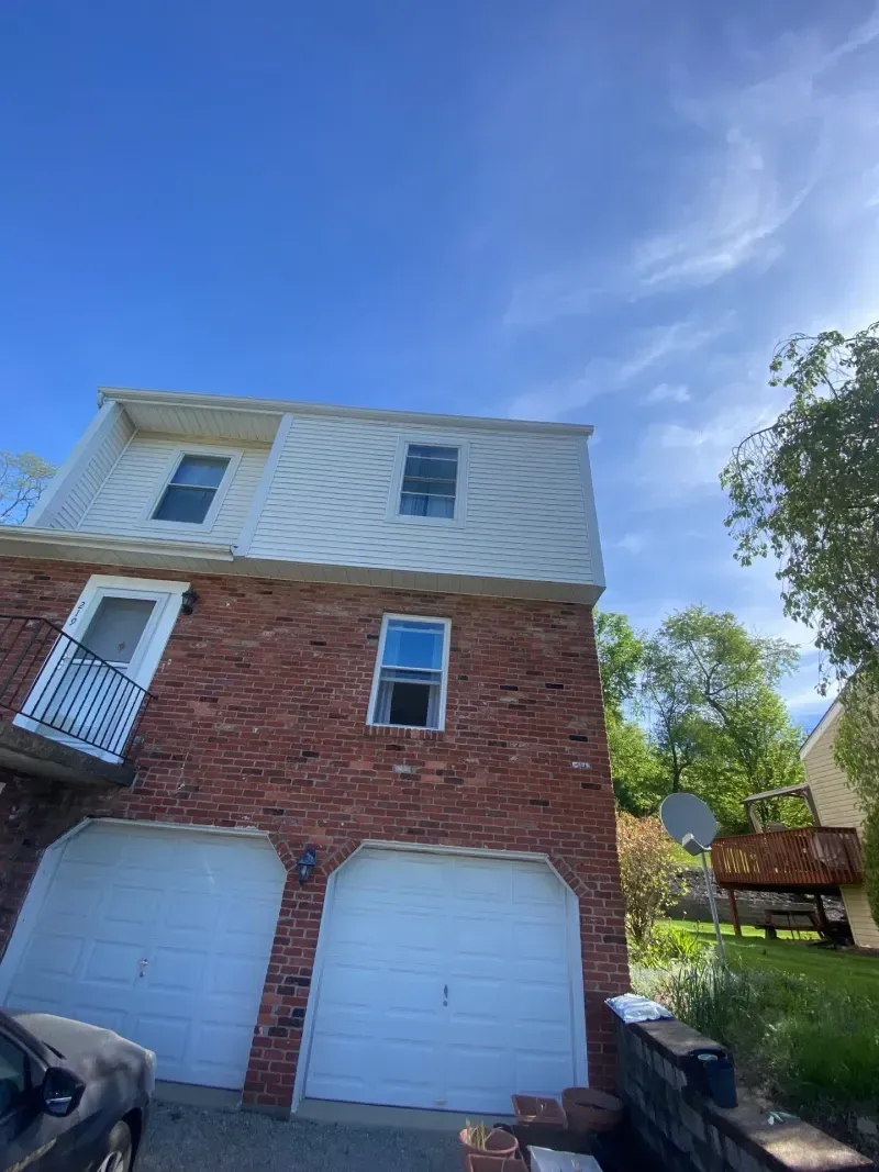 Brick house with white garage doors, windows, and balcony under a blue sky.