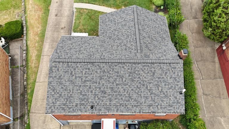 Brown asphalt shingle roof, some shingles are curling upwards, house exterior.