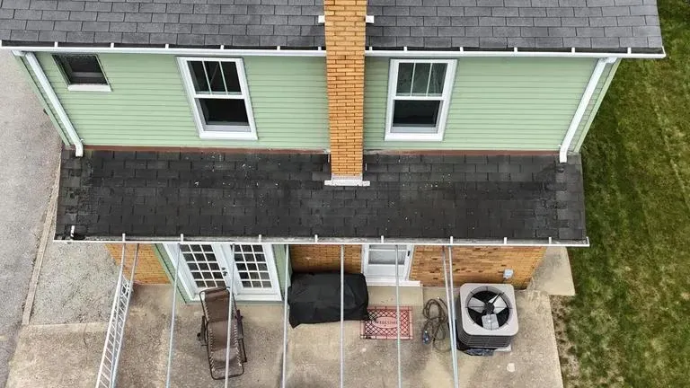 Overhead view of a house with a green exterior, chimney, and patio with furniture.