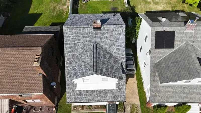 Overhead view of several houses; center house has gray roof with chimney. Car parked in driveway.