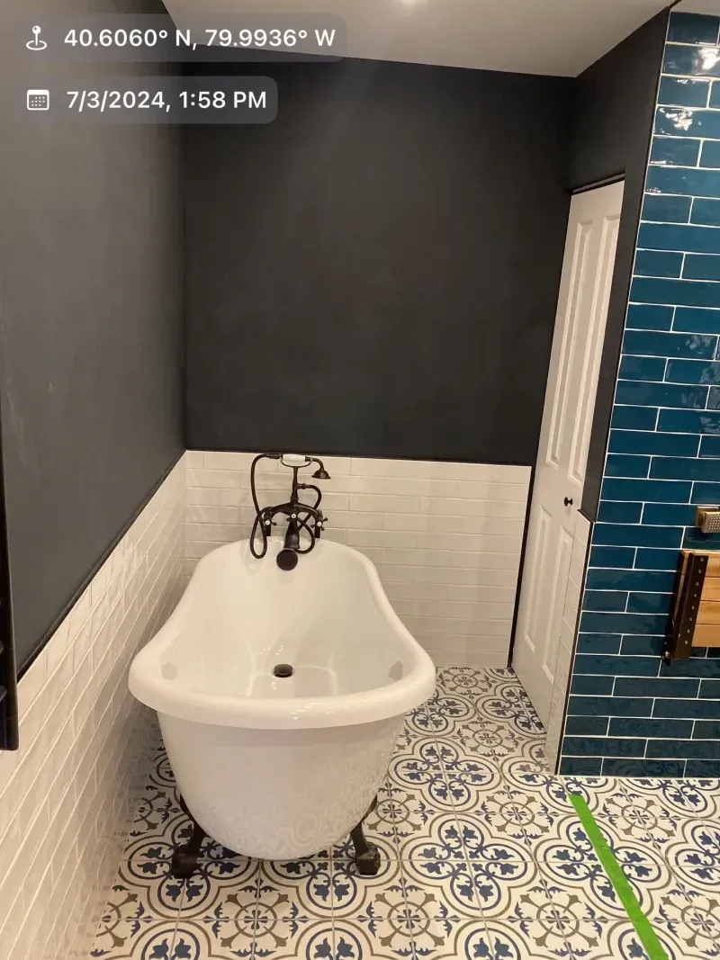 Clawfoot tub in a bathroom with dark grey and teal walls and patterned floor tiles.