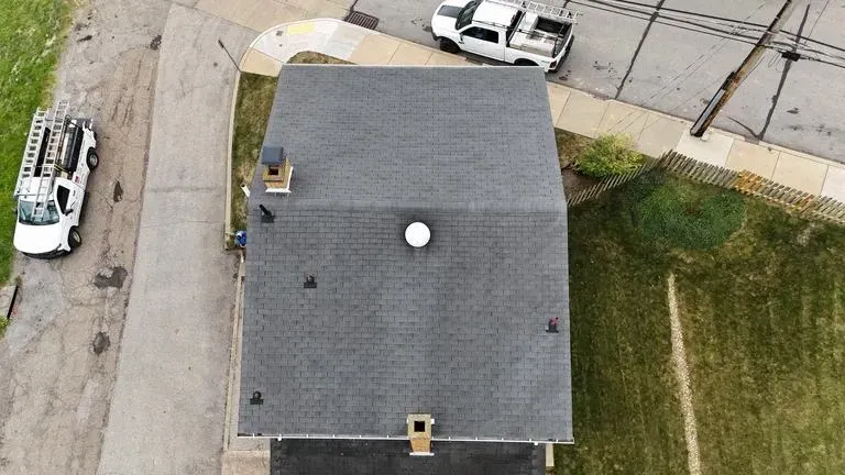 Overhead view of a house roof with a vent and chimney, parked vehicles on either side.