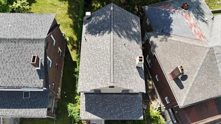 Overhead view of three houses with gray and brown roofs, surrounded by green trees.