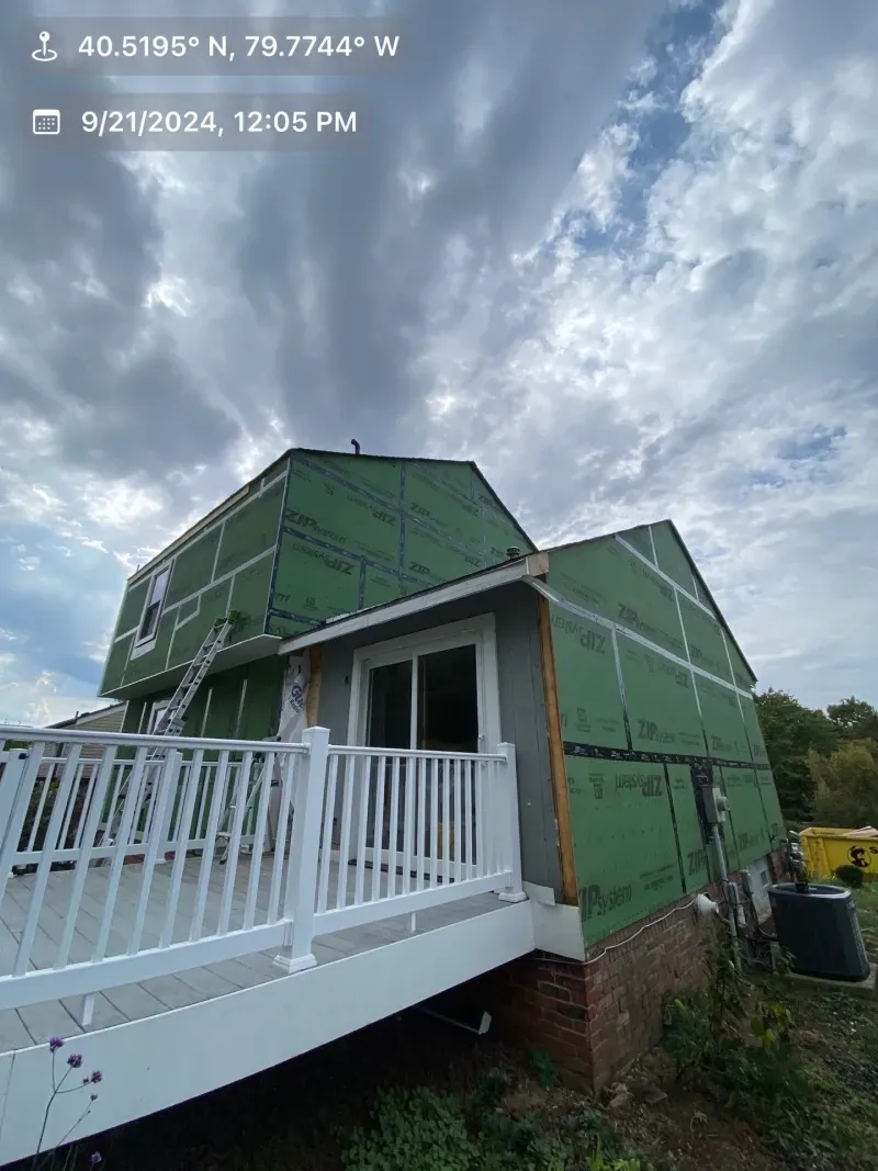 House under construction, green sheathing, white deck, cloudy sky.
