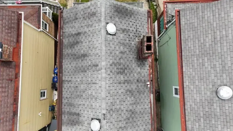 Overhead view of a gray asphalt shingle roof between two buildings, one tan and one green.