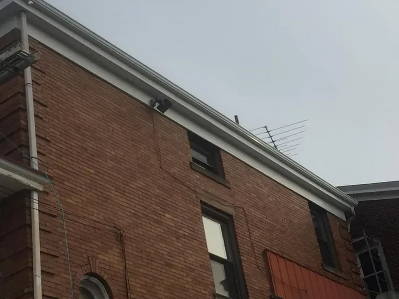 Brick building exterior with white trim, gutters, and an antenna. Overcast sky.