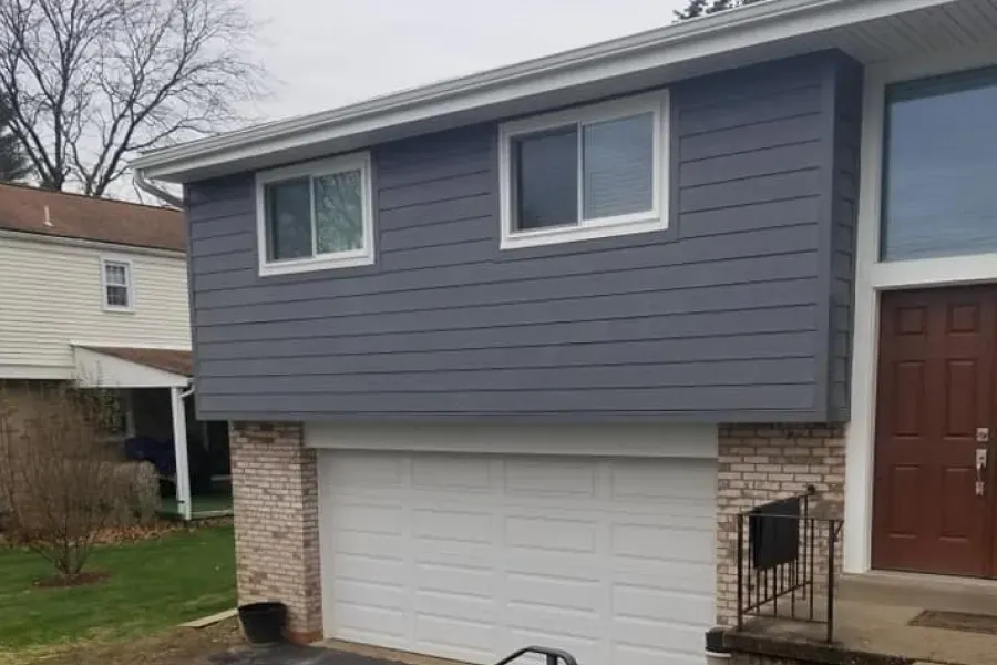 Gray house with white-framed windows above a white garage door, with brick accents.