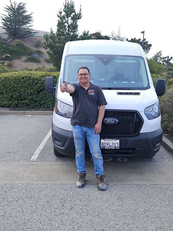 A man is standing in front of a white van and giving a thumbs up.