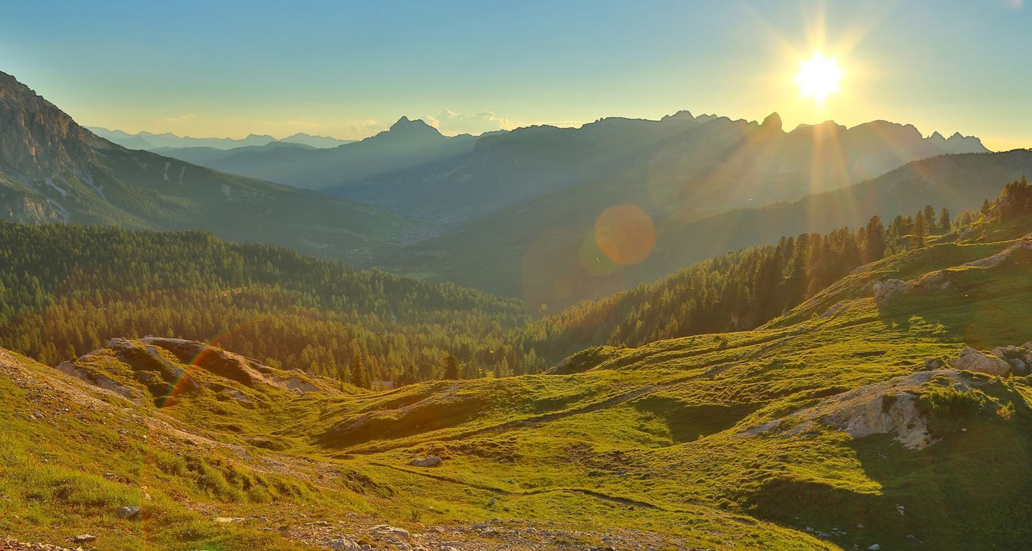 The sun is setting over a grassy hillside in the mountains.