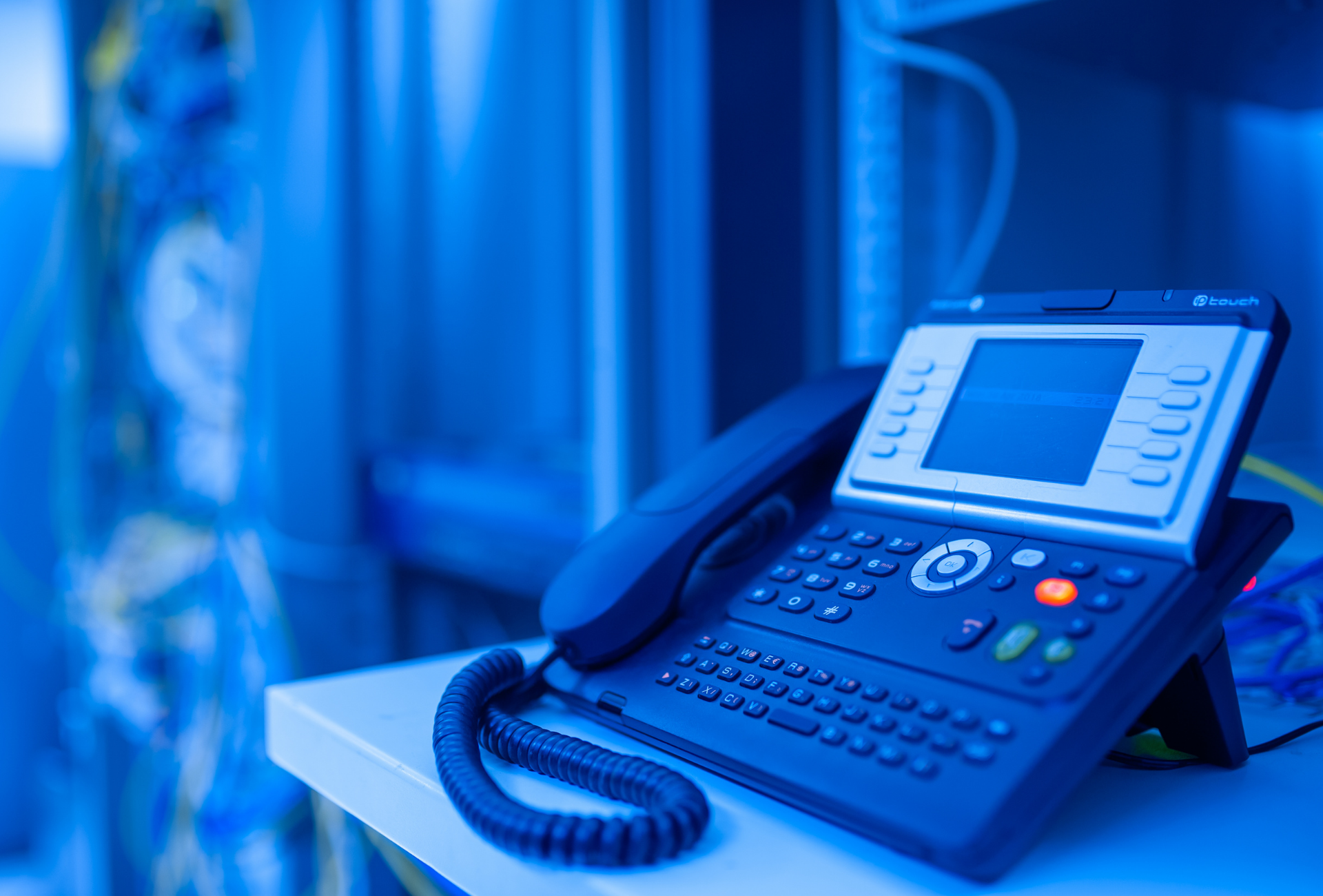 A business phone on a shelf in a server room, illuminated by blue lighting.