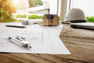 A wooden table topped with drawings , a compass , and a model house.