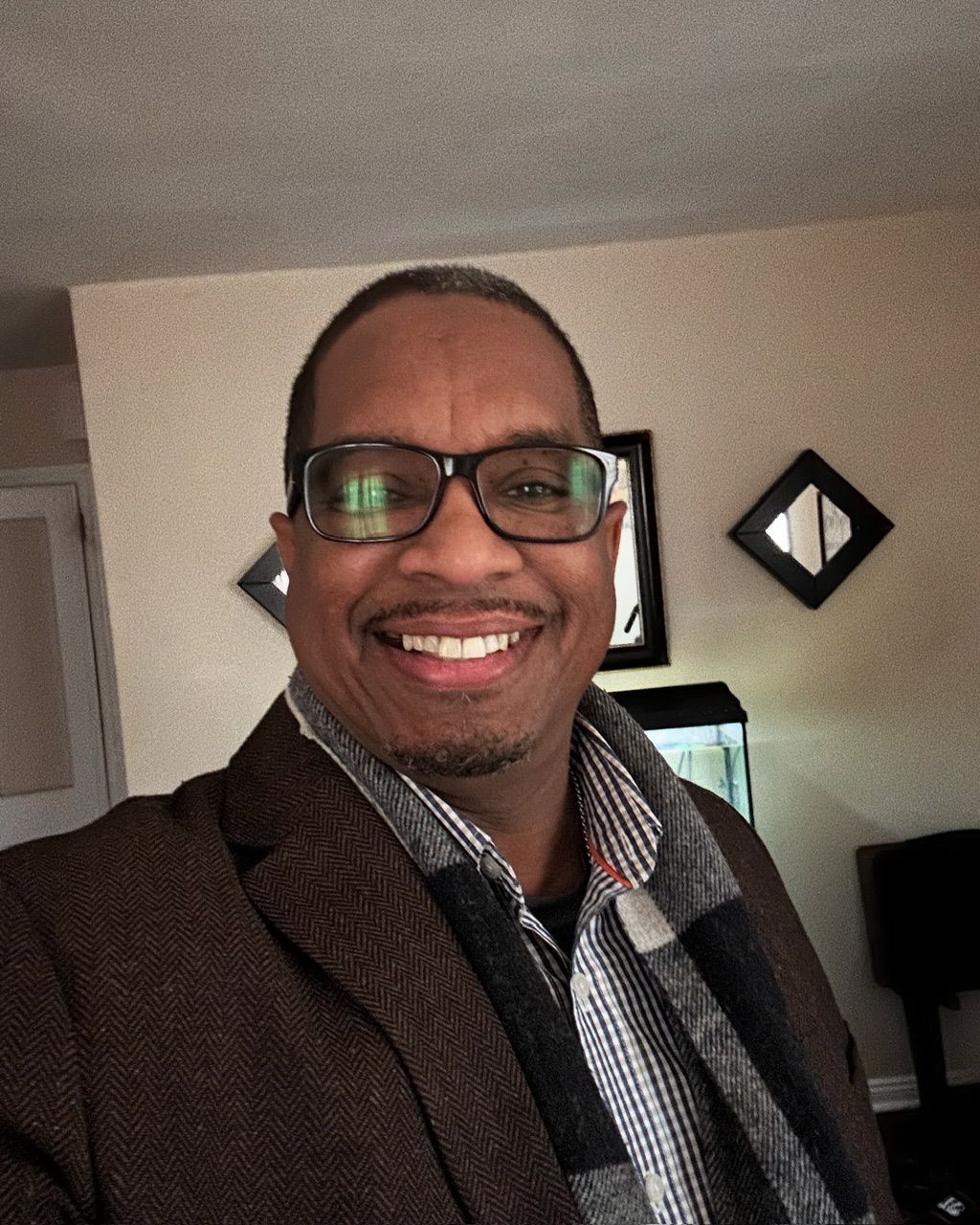 A man wearing glasses and a plaid shirt smiles for the camera