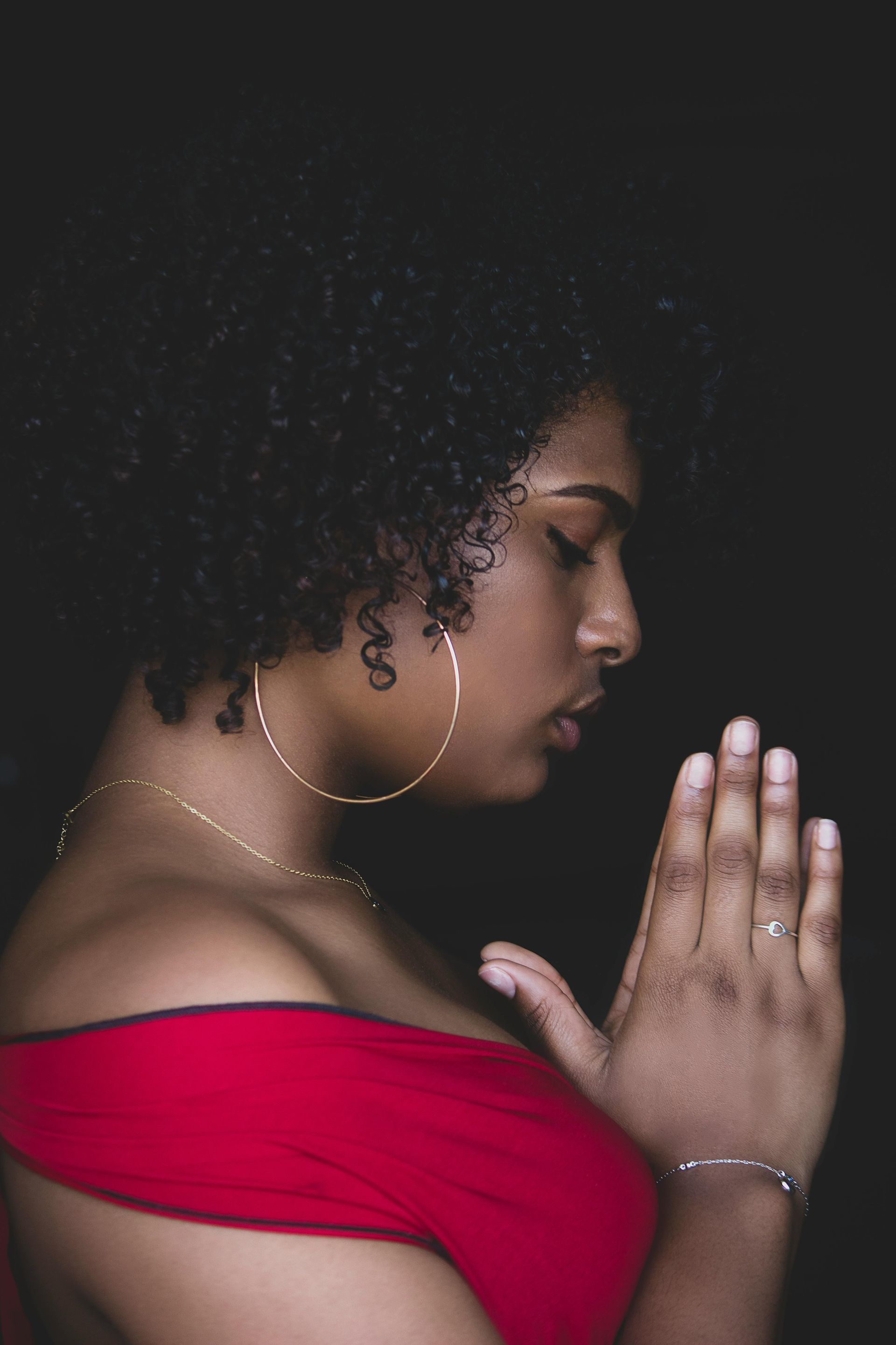 A woman in a red dress is praying with her hands folded.