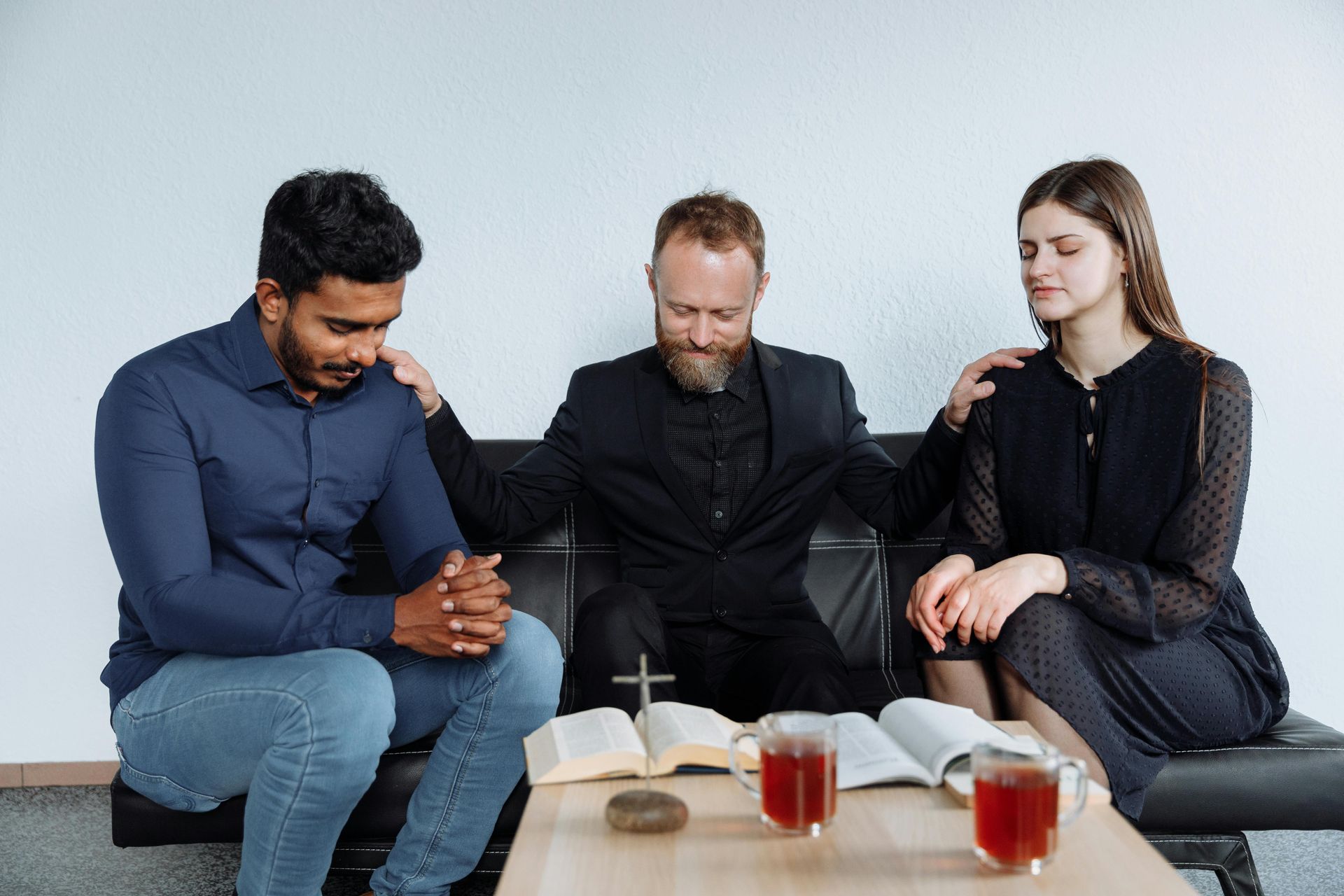 A group of people are sitting on a couch praying together.