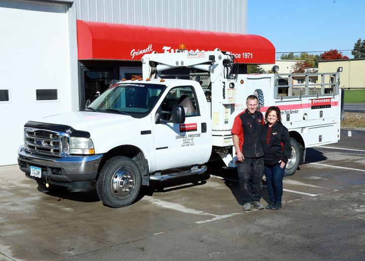 A white service truck with two people posing outside a building with a red awning.