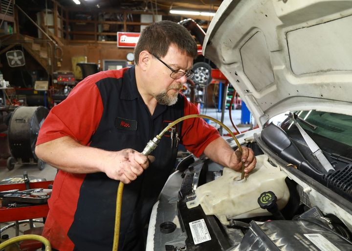 Mechanic working on a vehicle's engine, holding a hose in a garage.