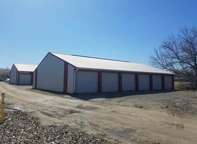 Storage units with gray doors and red trim under a blue sky. Gravel lot.