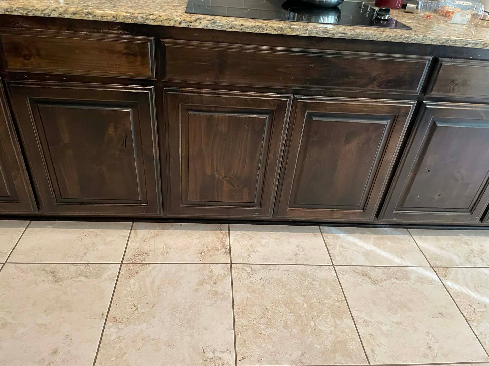 Dark wood kitchen cabinets above beige tile flooring.