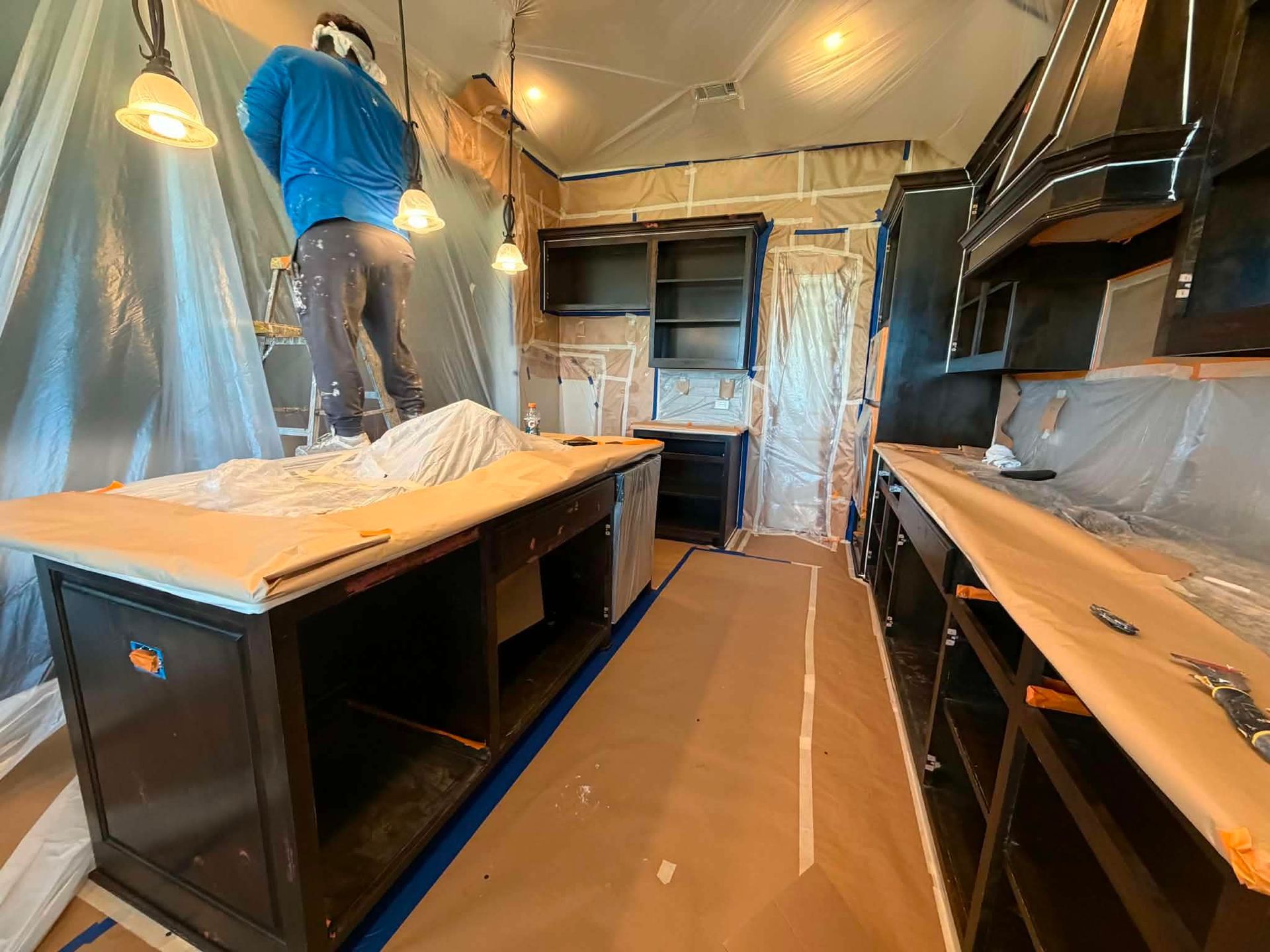 Kitchen under renovation with plastic sheeting, workbenches, and a worker on the left counter