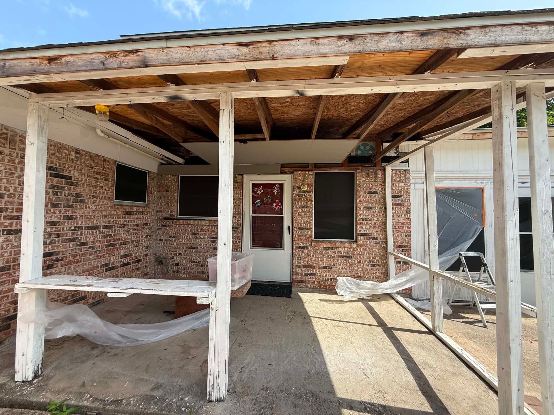 Front porch of an old brick house with a white-framed door, windows, and weathered wooden beams.