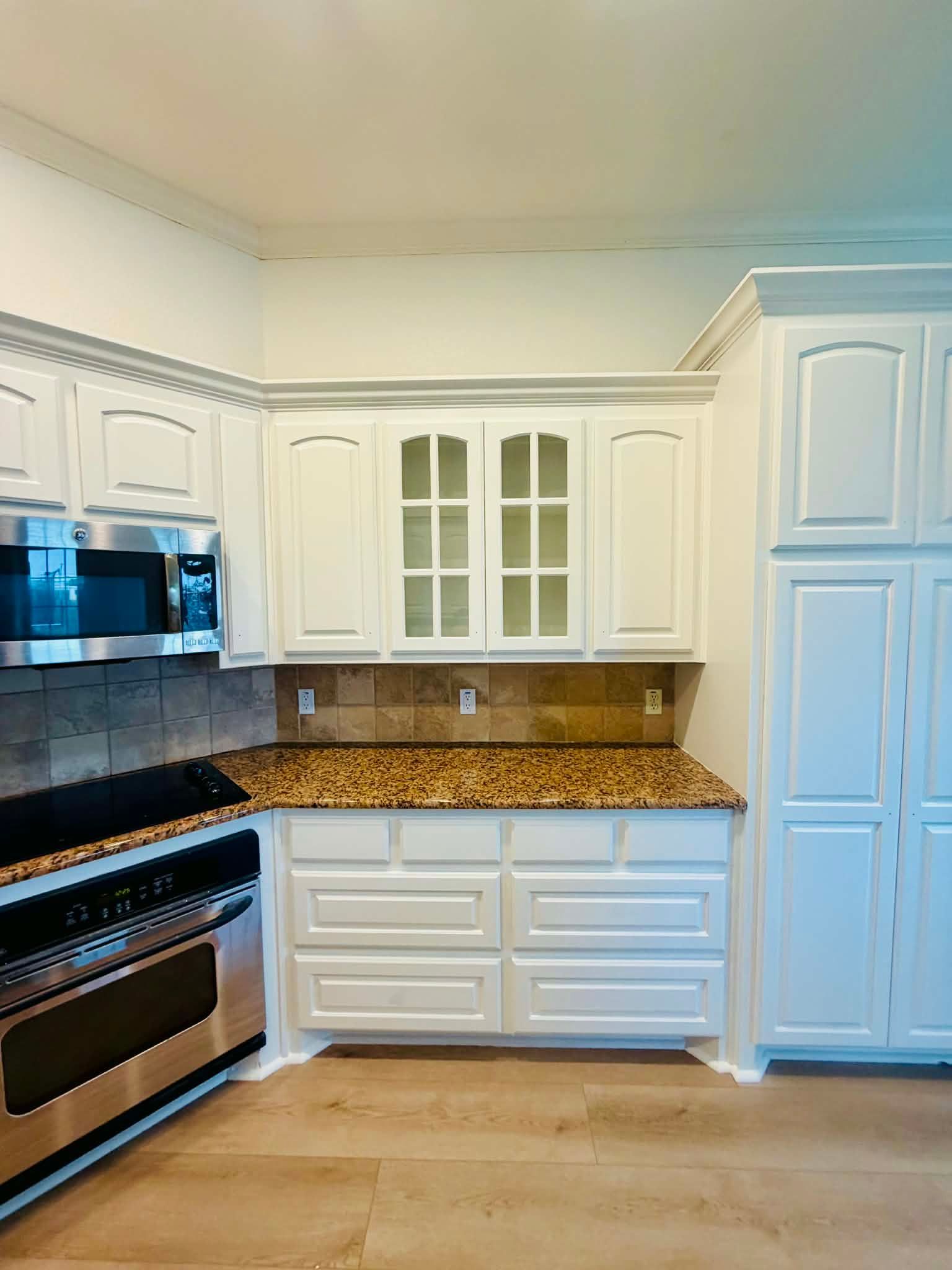 White kitchen with stainless steel stove and microwave, white cabinets, and granite countertops