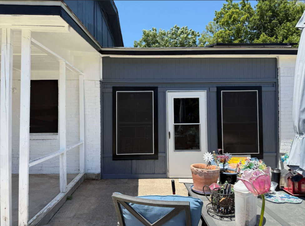Patio with outdoor chairs and potted plants beside a dark gray house exterior with white trim
