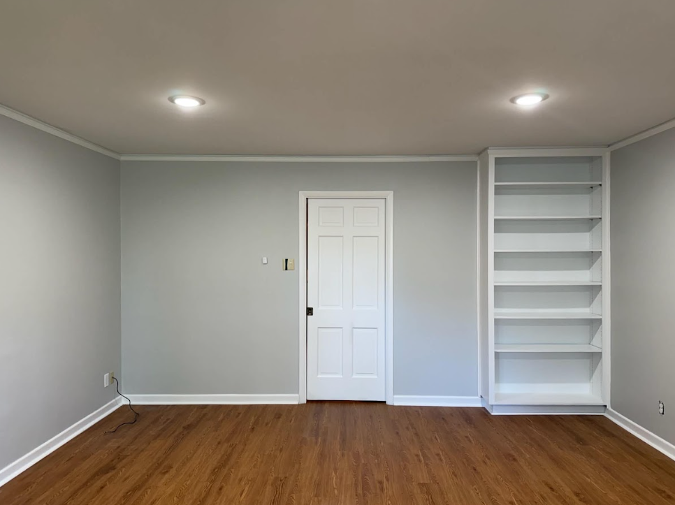 Empty room with gray walls, white door, hardwood floor, recessed lights, and built-in shelves.
