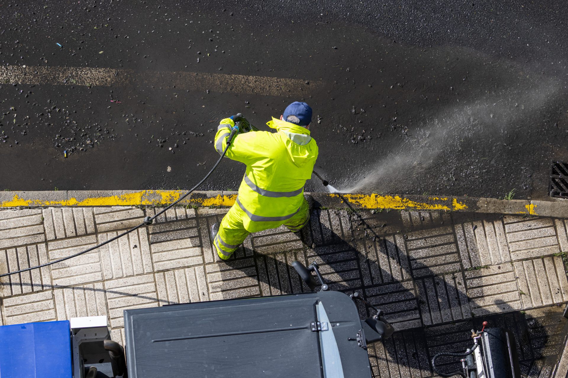 Worker in neon yellow safety gear cleaning a wet street beside a curb