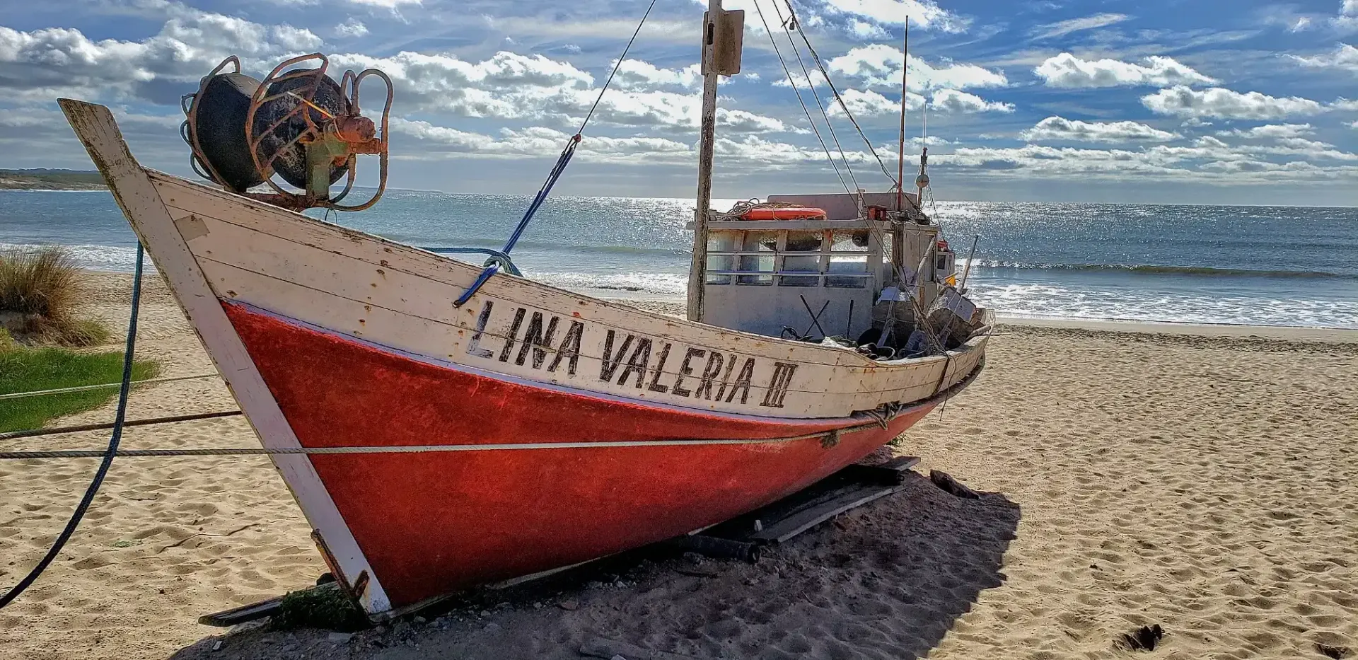 A red and white boat is sitting on a sandy beach near the ocean.